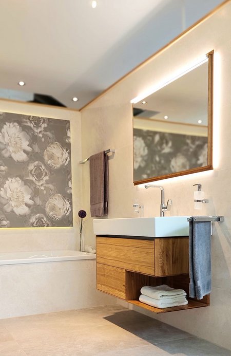Modernes Badstudio mit floraler Wandgestaltung, eingelassener Badewanne, beleuchtetem Spiegel und Waschtisch aus Holz mit Handtüchern.